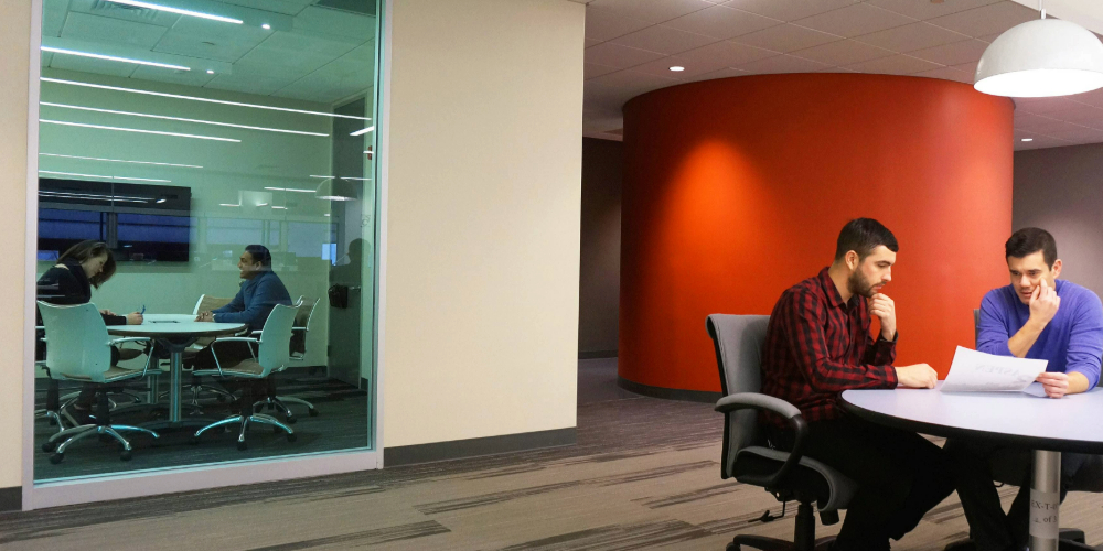 Two people meet in a privacy room behind a window, while two other people meet in a common area.