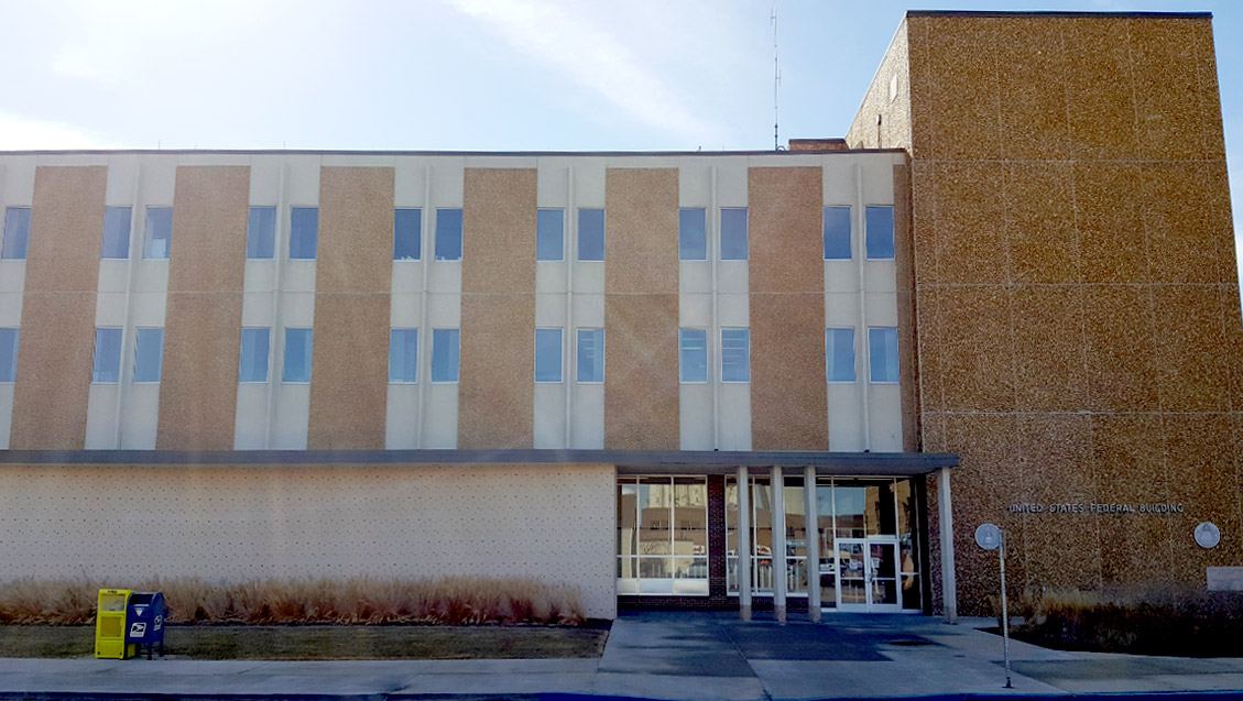 A backlit view of a 3-story blonde brick building with the words United States Federal Building on it.